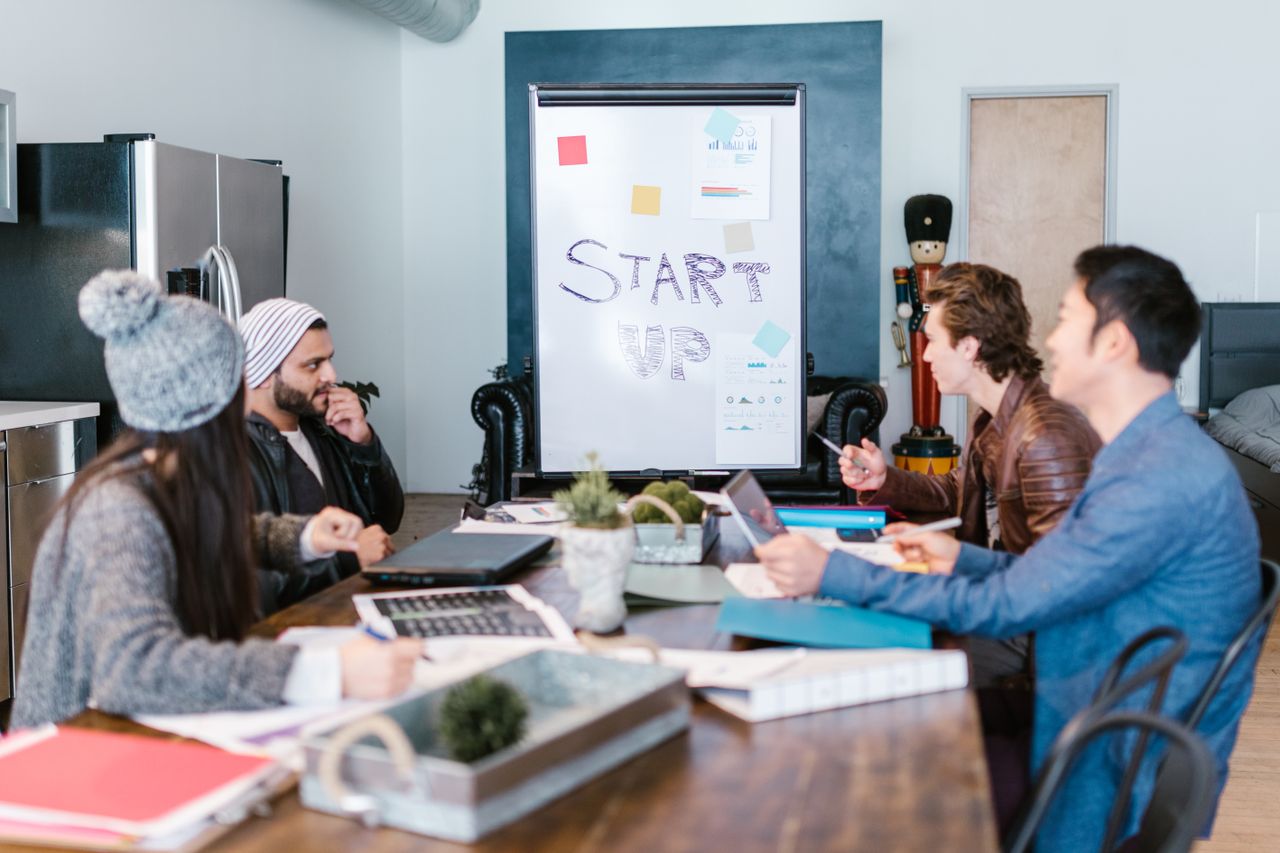 Services A diverse group of adults working around a table in a startup office, planning and discussing ideas.